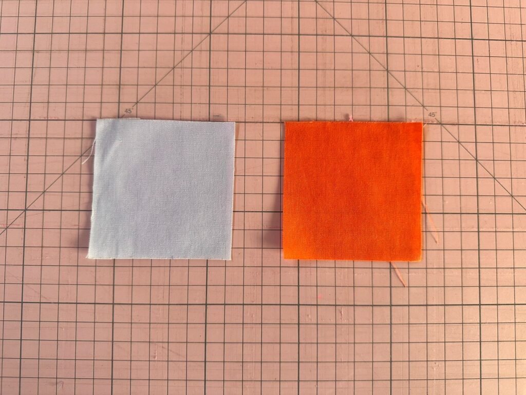 2 quadrados de tecido em cima de uma base de corte pra fazer patchwork.